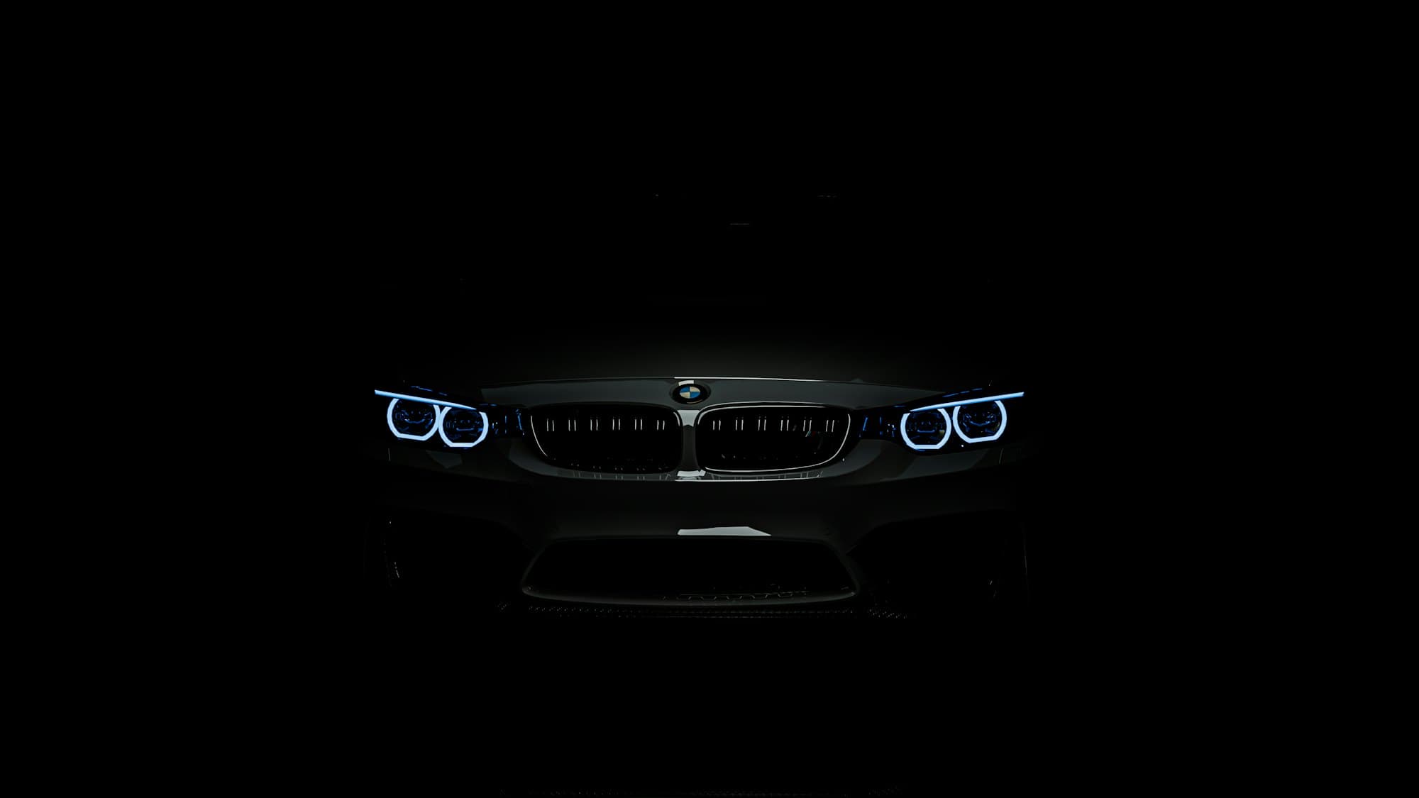 A BMW M4 in total darkness: only its four ring-shaped headlights and twin grille are visible