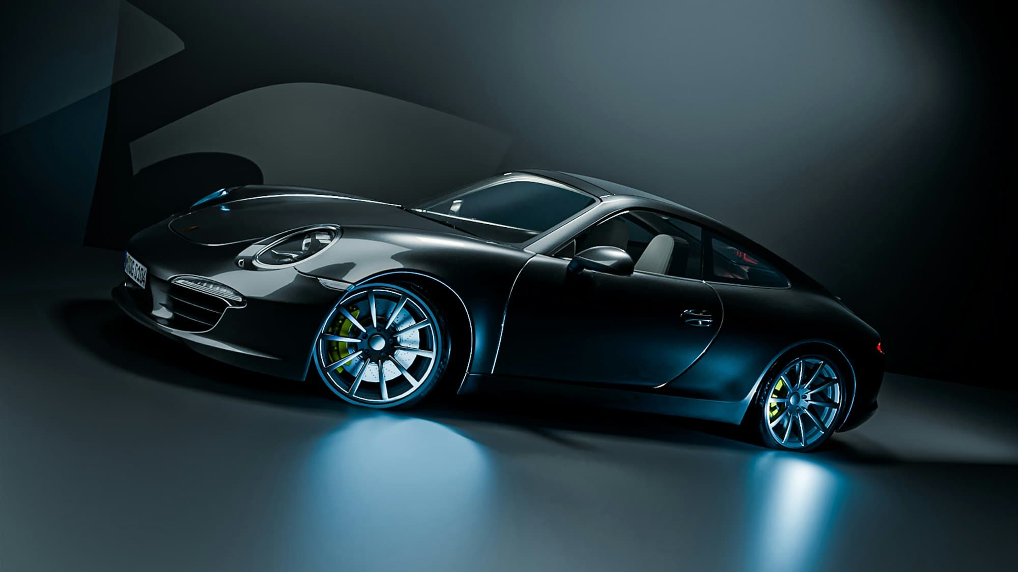 Black Porsche 911 in a dark studio, its centre-lock wheels lit ice blue from the floor