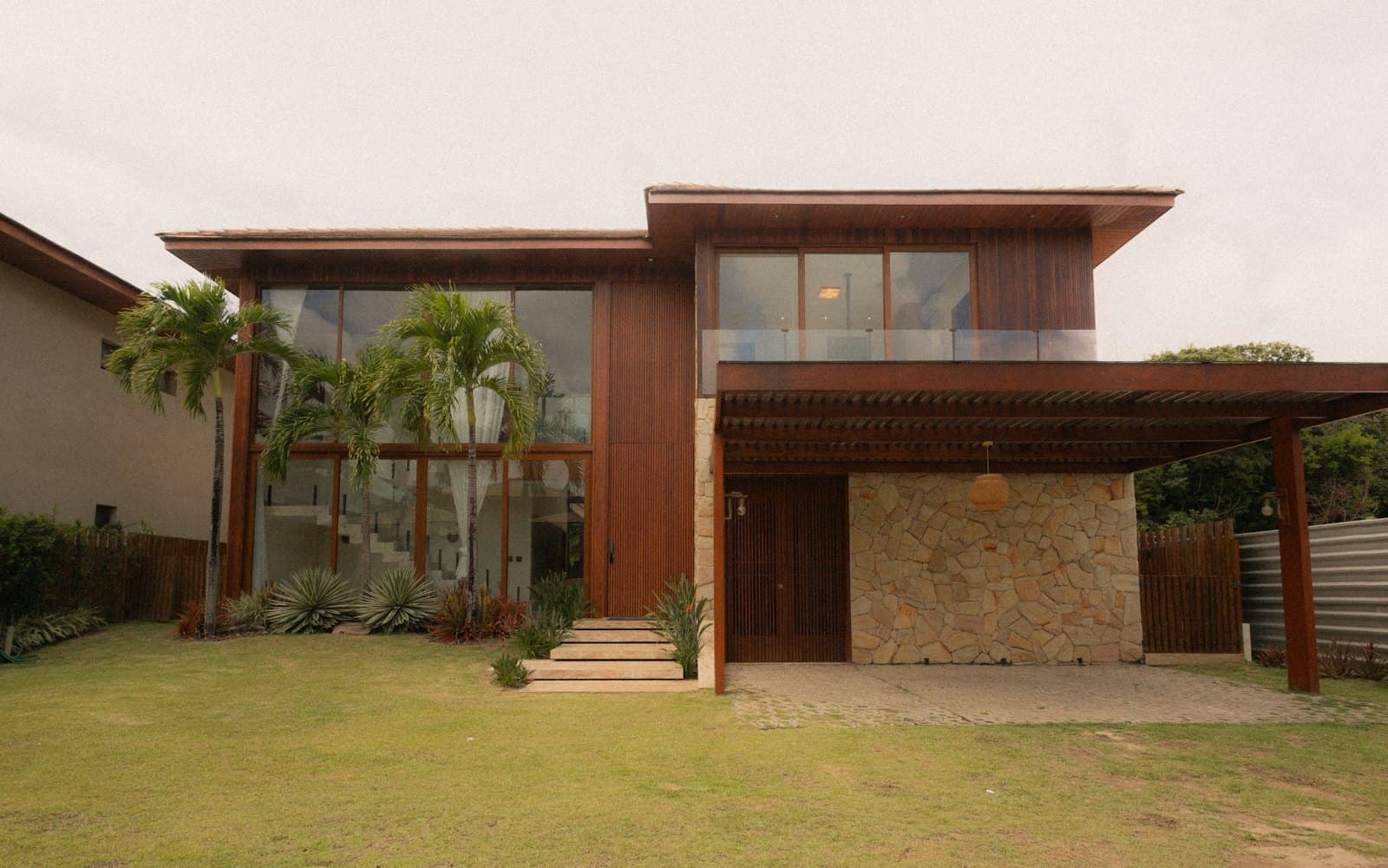 A finished two-storey house with timber cladding, tall windows, a stone ground floor and a carport
