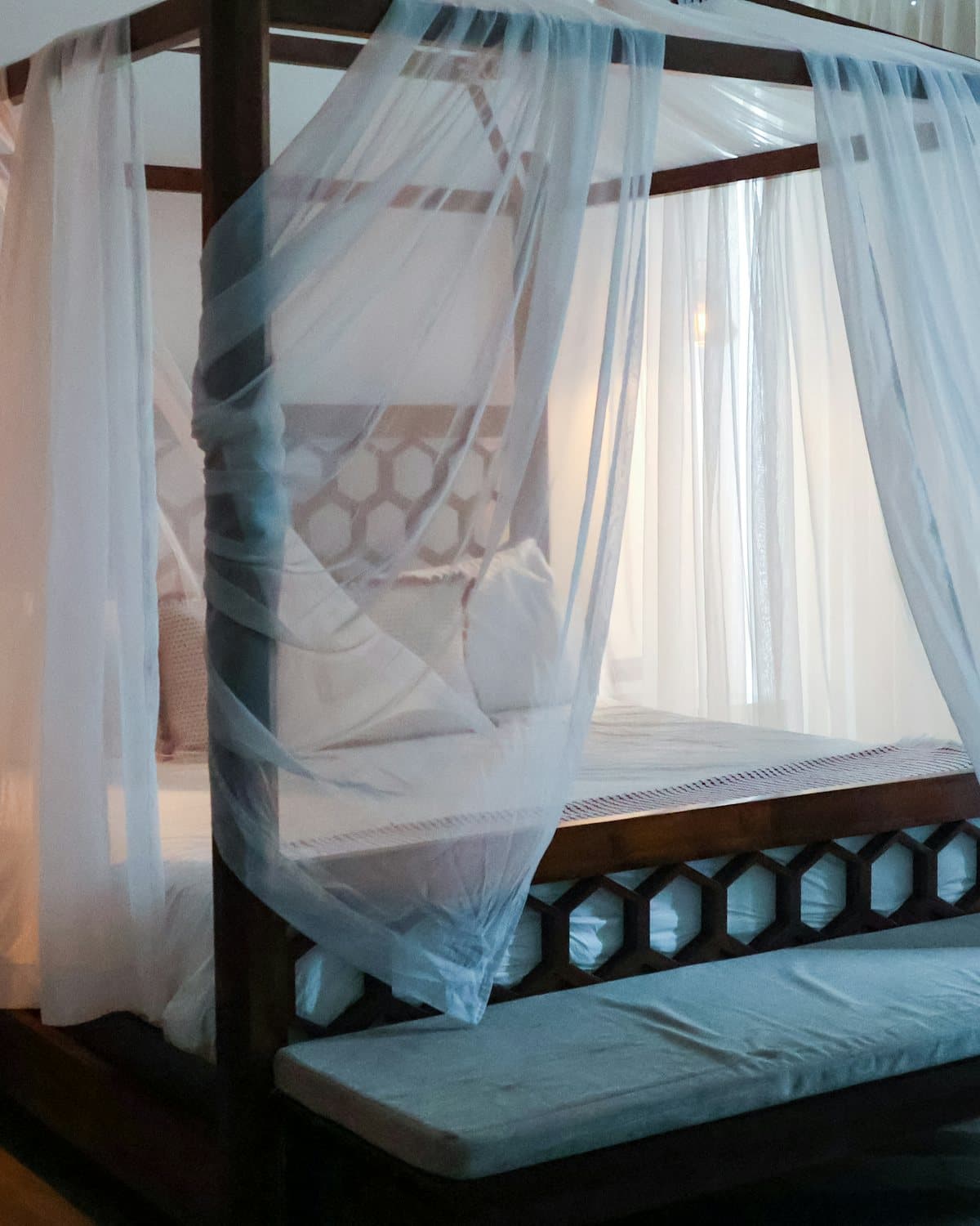 A four-poster bed veiled in white muslin, lit by a single hanging lamp
