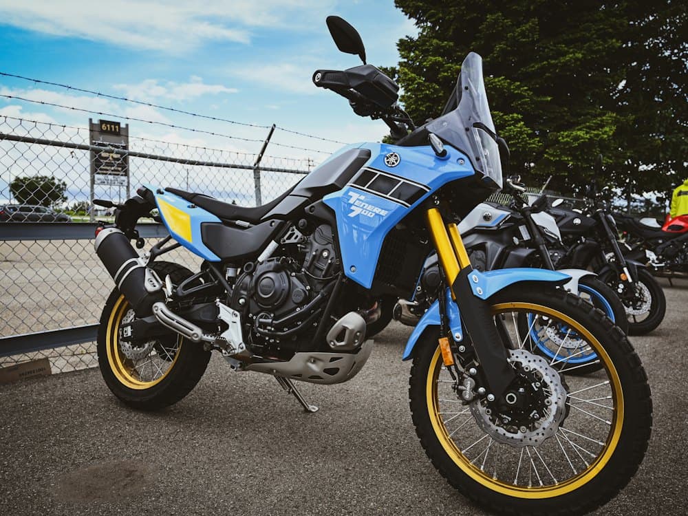 A light blue Yamaha Ténéré 700 with gold wheel rims and a yellow fork, parked on tarmac