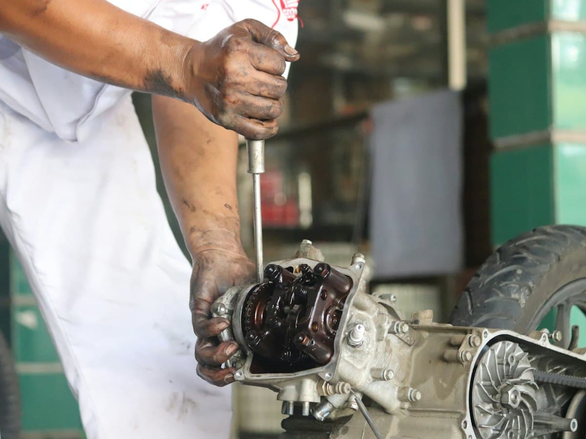A mechanic's oil-blackened hands working a screwdriver into a scooter engine casing