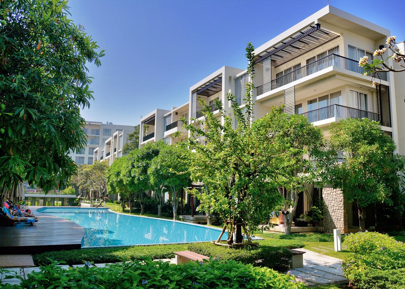 A low-rise apartment building with deep balconies around a long garden swimming pool