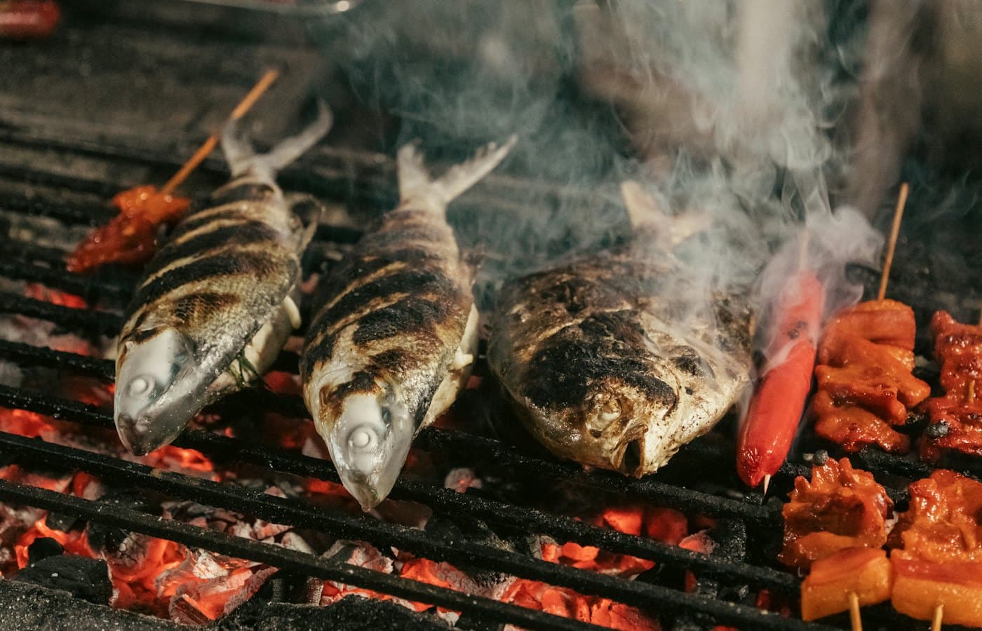 Whole fish charring on a grill over glowing charcoal, smoke rising