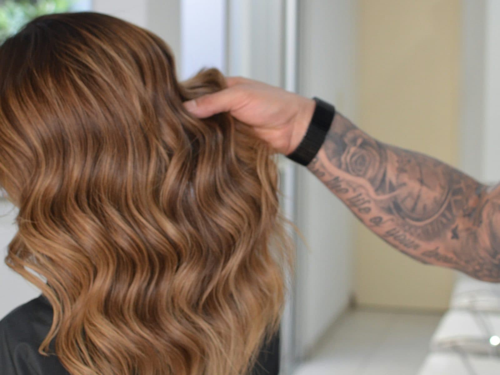 Shoulder-length copper-brown hair set in glossy brushed-out waves, a stylist’s hand lifting one side