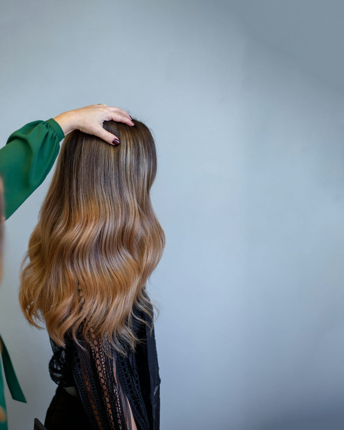 Long wavy hair fading from dark brown to honey at the ends, a hand resting on top of the head
