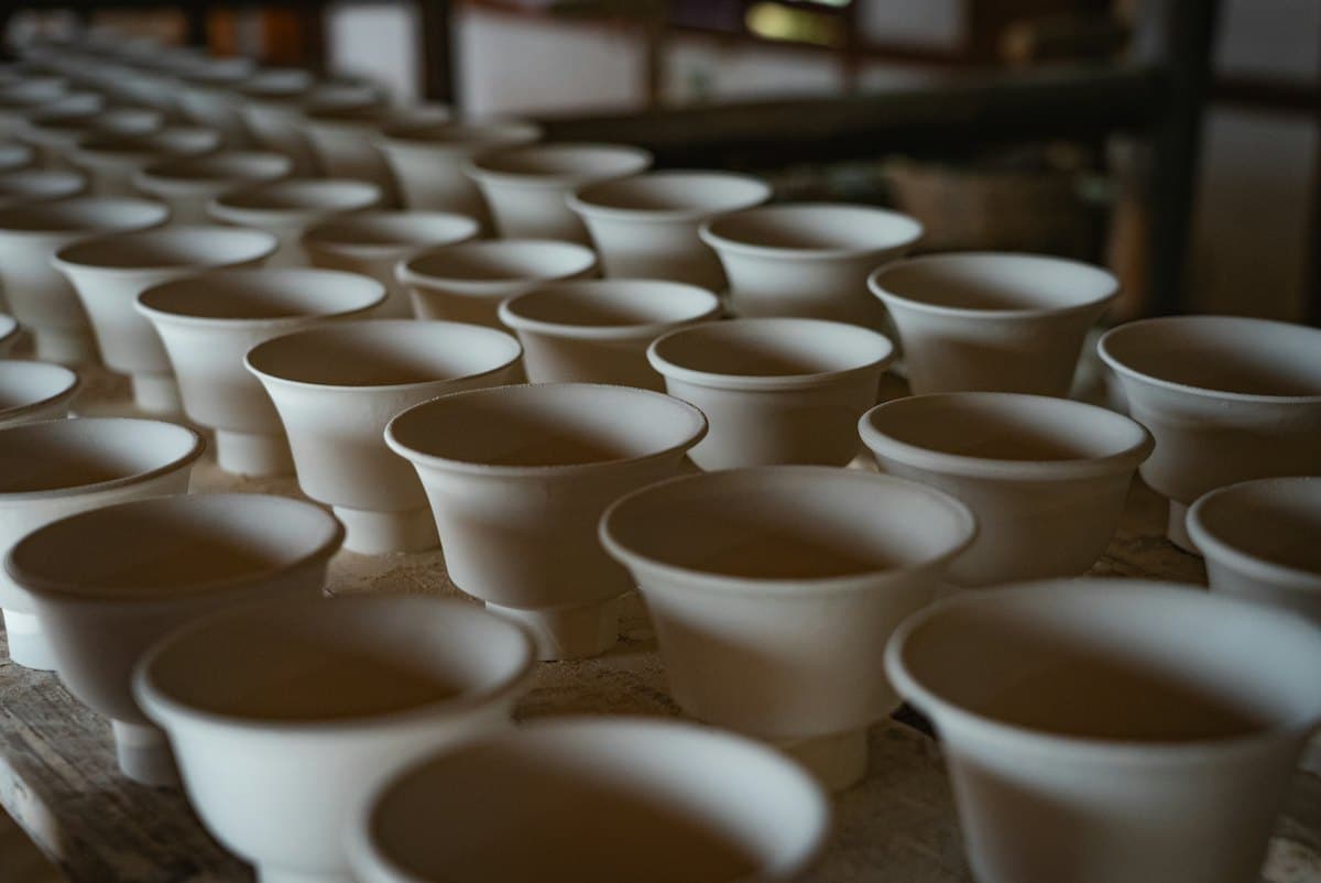 Rows of unglazed footed cups drying on a wooden board before their first firing