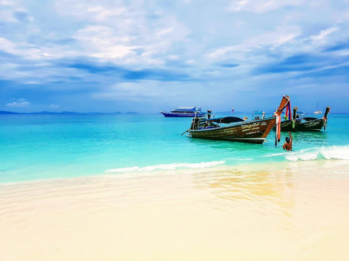 Two longtail boats anchored off an empty white-sand beach