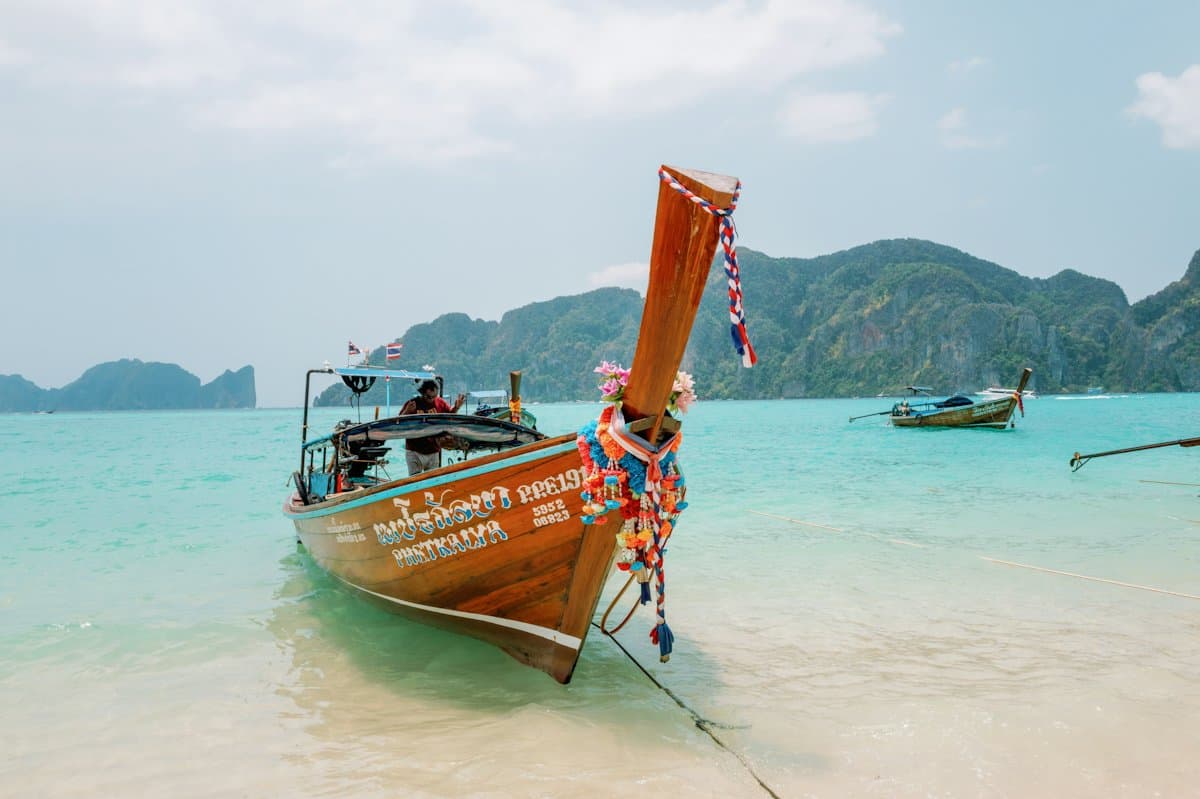 A wooden longtail boat with garlands on its prow, resting in clear shallow water