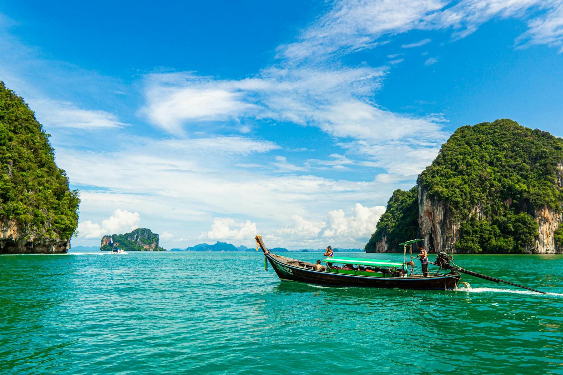A longtail boat crossing bright turquoise water between jungle-covered limestone islands