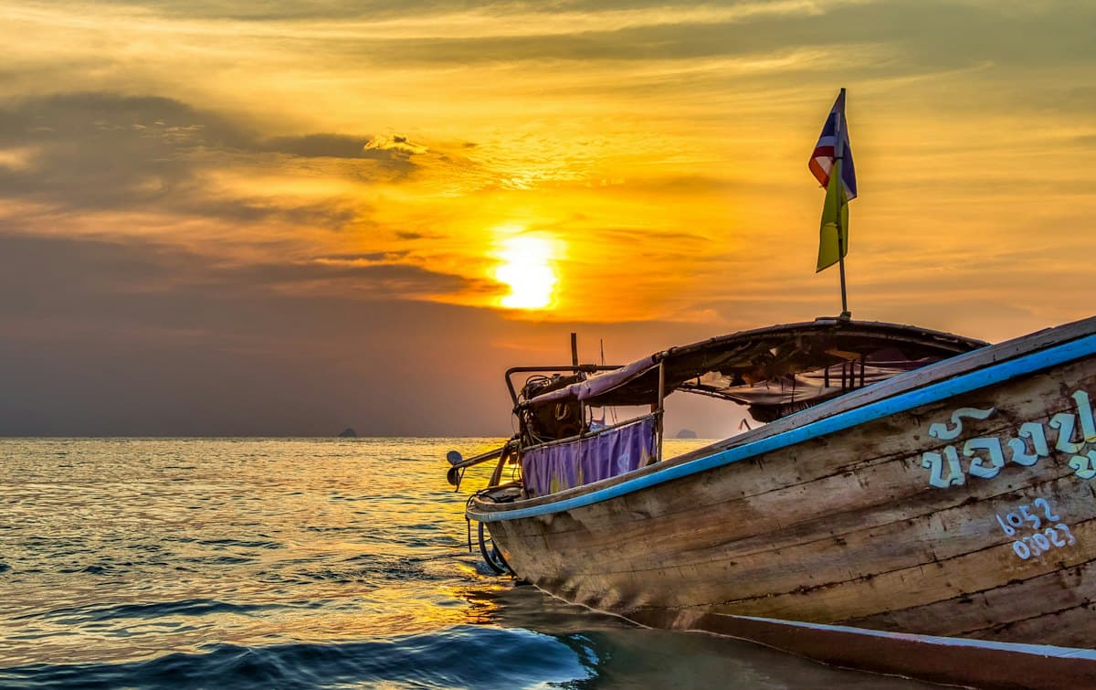 The prow of a longtail boat on the water as the sun sets behind it
